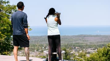 Two people standing on a wooden deck overlooking a scenic landscape with a clear view of the sea and distant hills.