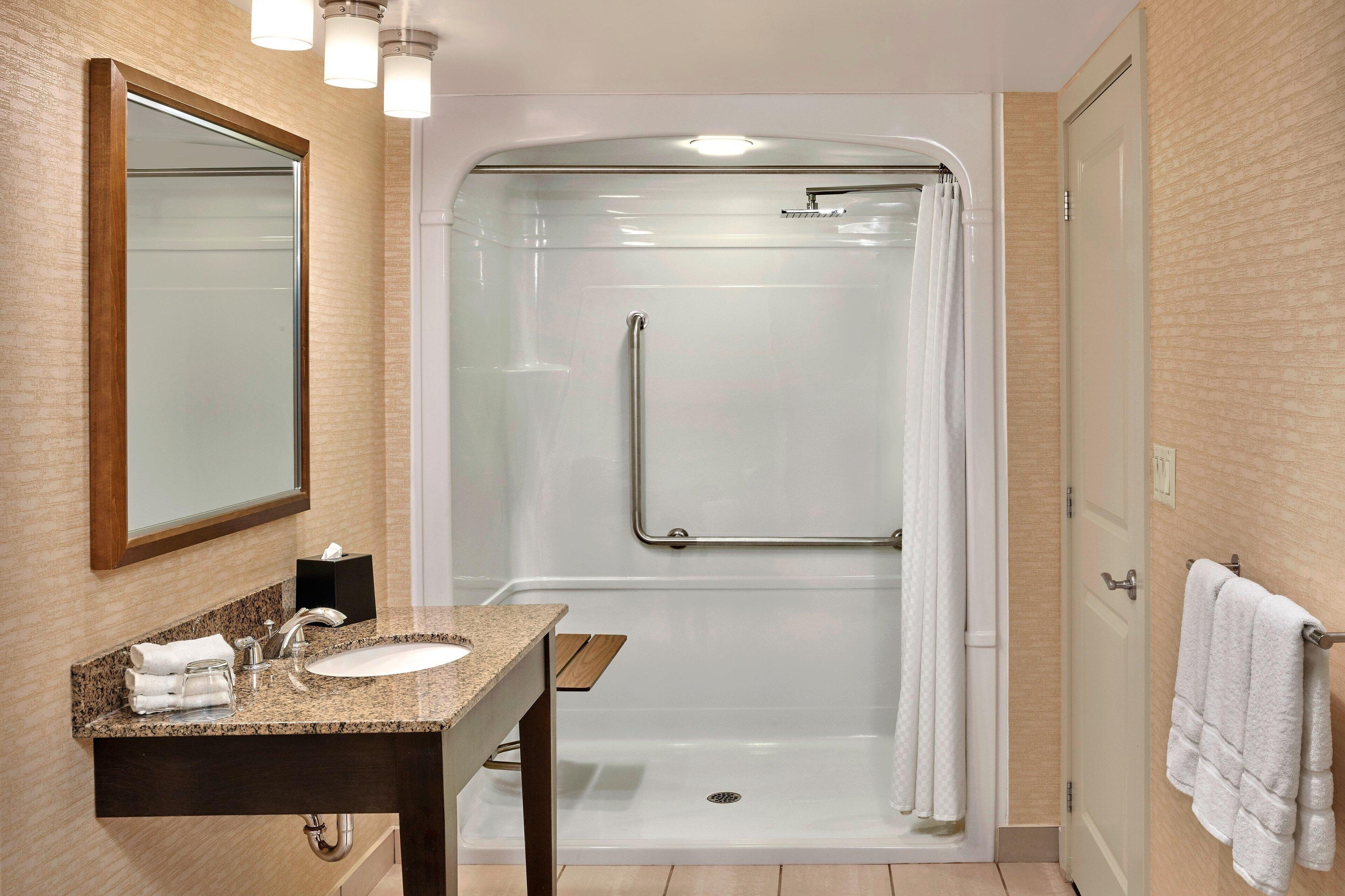 A modern bathroom with a granite sink, a glass shower enclosure, and a white towel rack.