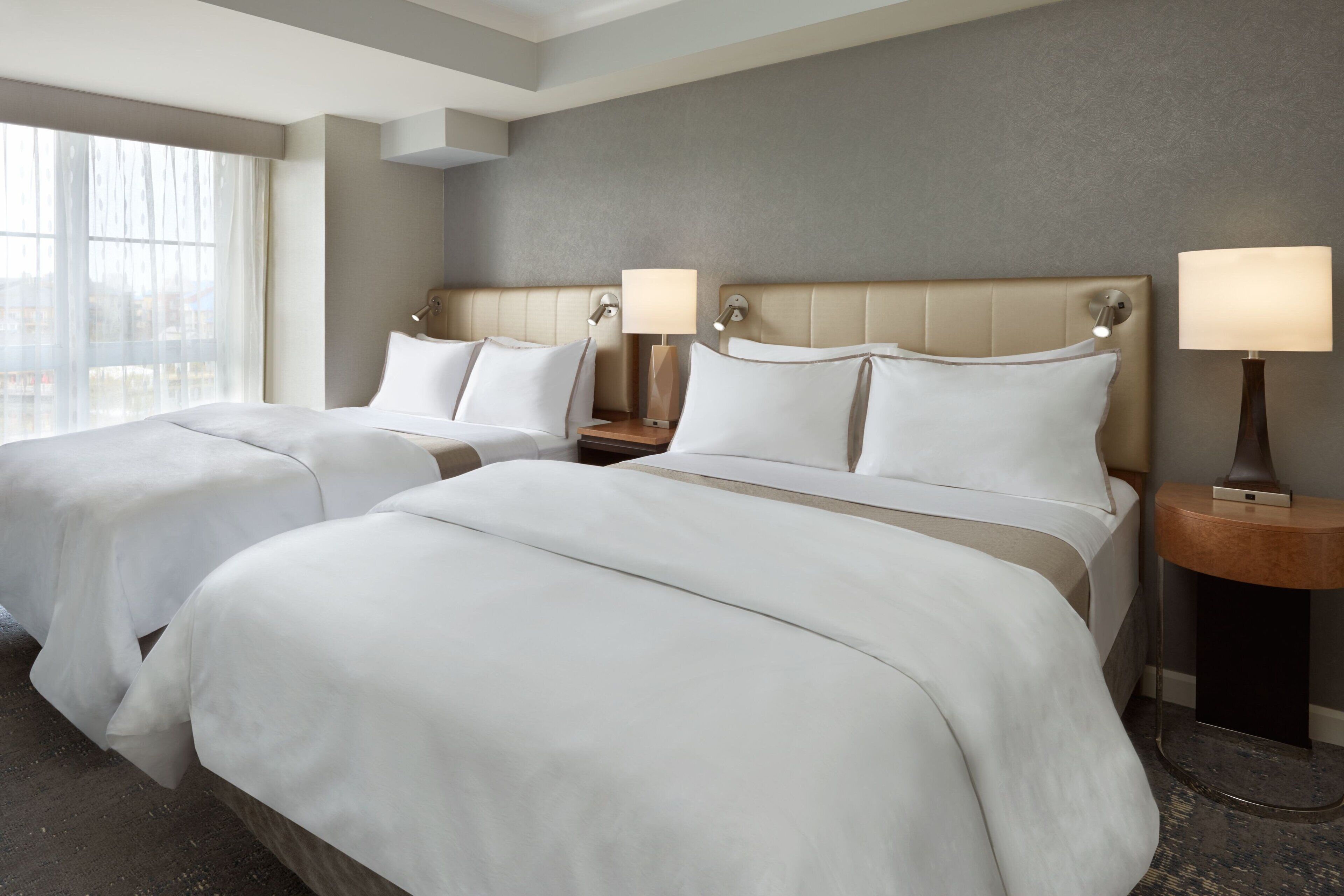 Een hotelkamer met twee bedden, een groot raam en een neutraal kleurenschema.
