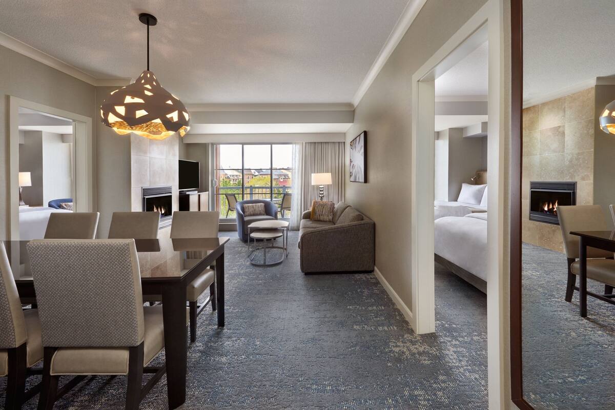 A hotel room with a dining area, a sofa, a bed, and a fireplace.