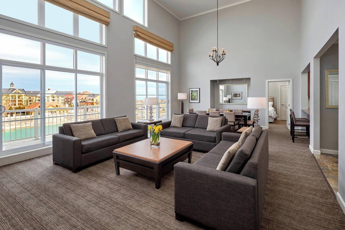 A spacious living room with large windows, a chandelier, and a view of a cityscape.