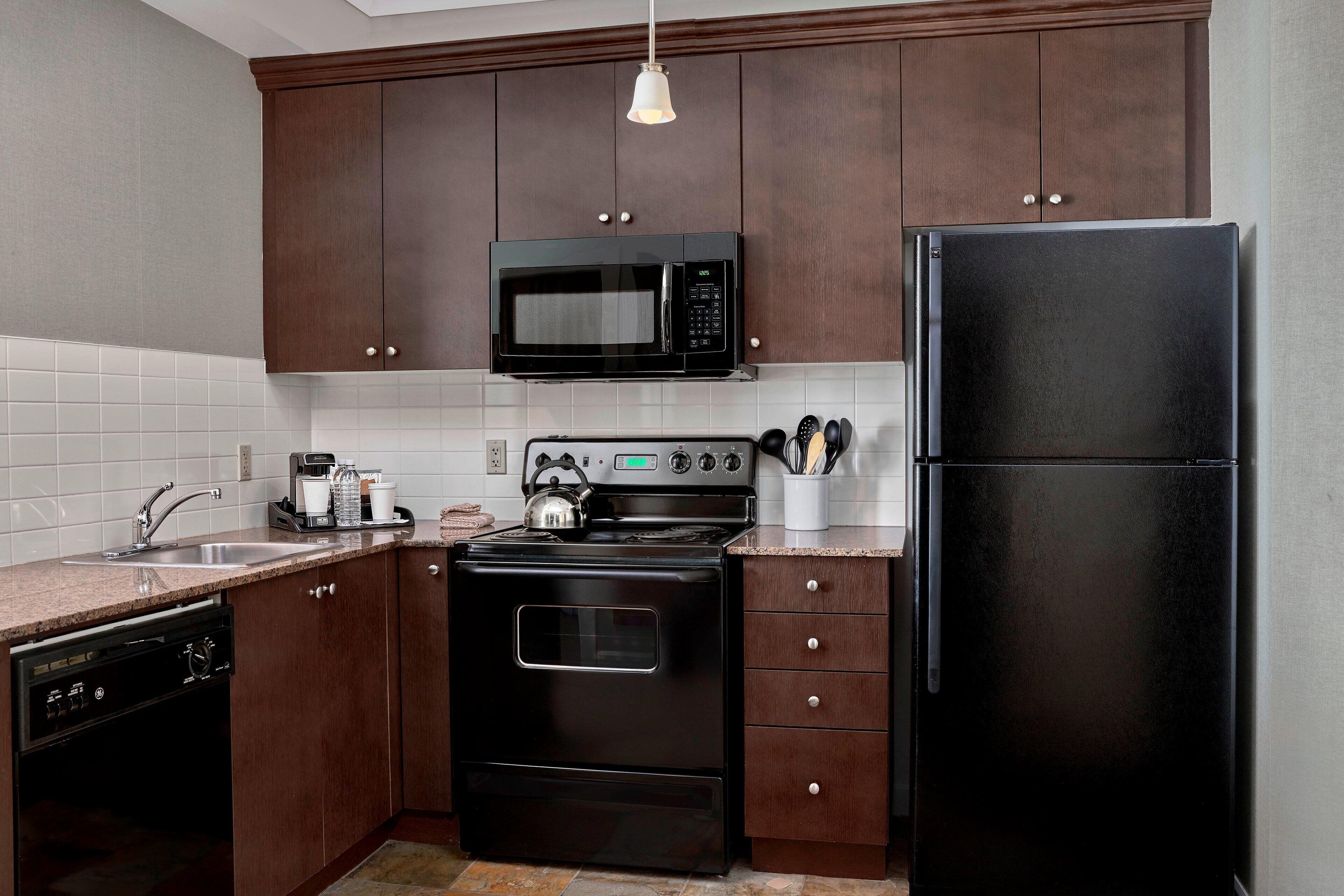 A kitchen with dark wooden cabinets, a black microwave, a black refrigerator, a stove, and a dishwasher.