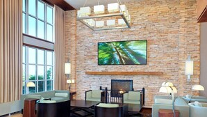 Un vestíbulo moderno con pared de piedra, un televisor de pantalla plana grande y una chimenea. Hay varias zonas de estar con sofás y sillones.