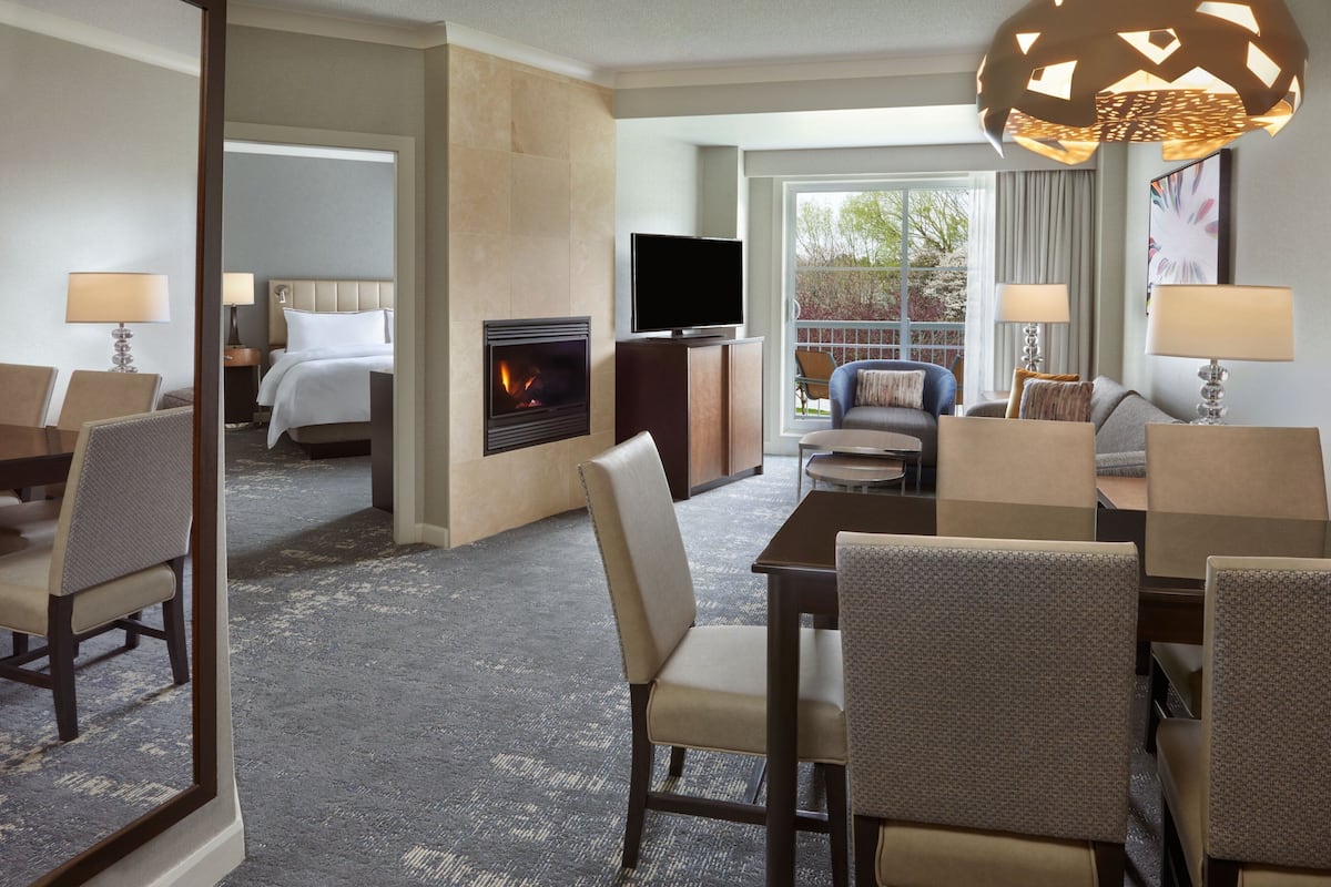 A hotel room with a fireplace, a TV, a dining area with chairs, and a view of the outdoors.