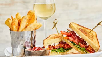 Ein Teller mit einem gegrillten Sandwich, einem Glas Weißwein und einer Portion Pommes.