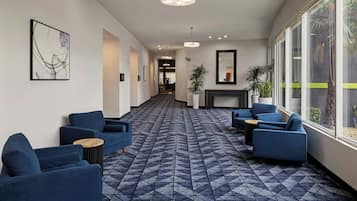 A hotel lobby with a geometric patterned carpet, blue seating, large windows, and a fireplace.