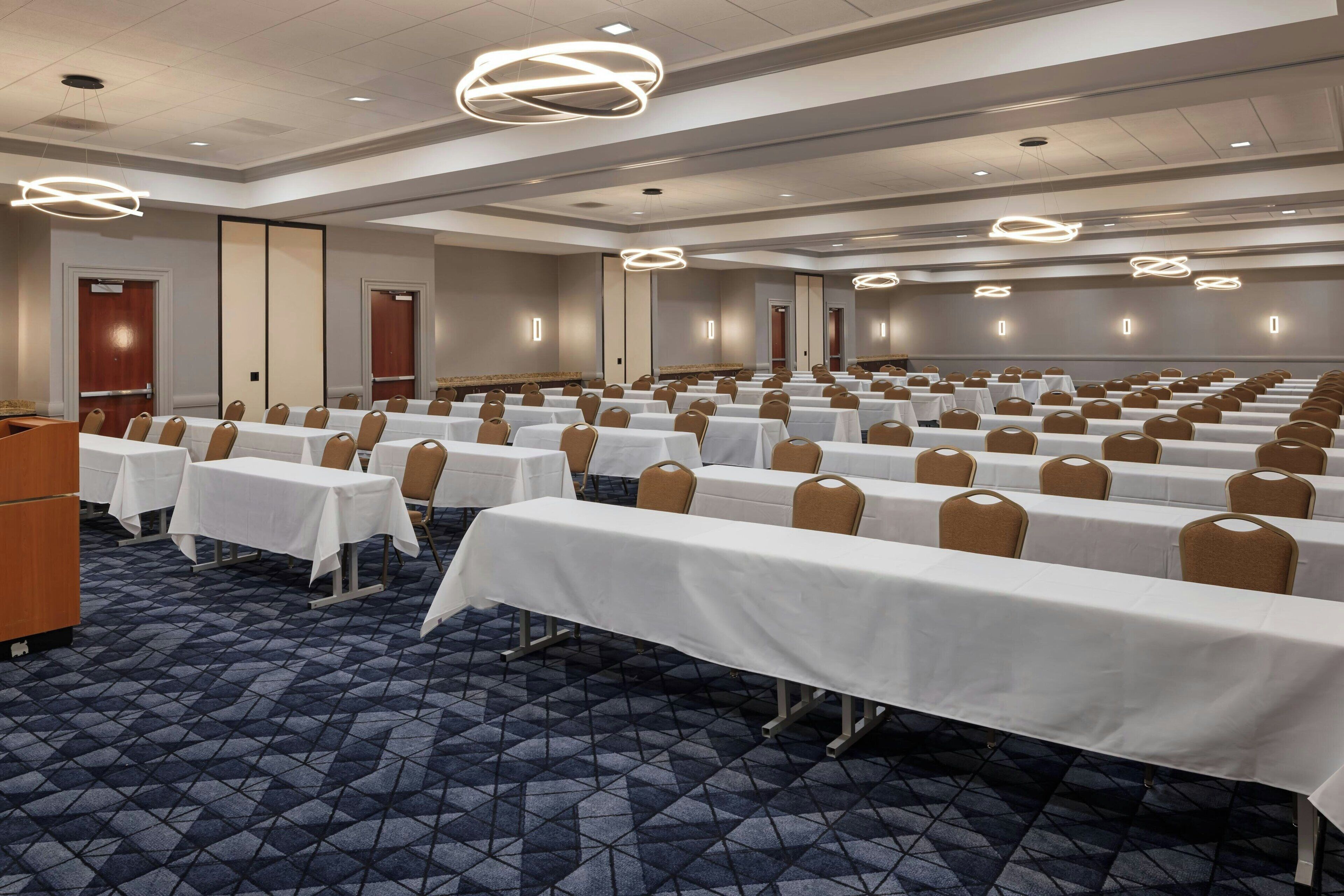 A conference room with rows of tables and chairs, a patterned carpet, and modern lighting fixtures.
