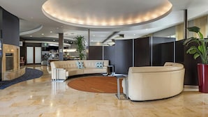 Un lobby moderno con un sofá curvo, una mesa redonda de madera y una planta grande en maceta.