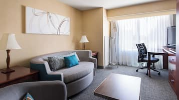 Habitación de hotel con sofá, sillones, una mesa de centro, televisor, escritorio y ventana con cortinas.