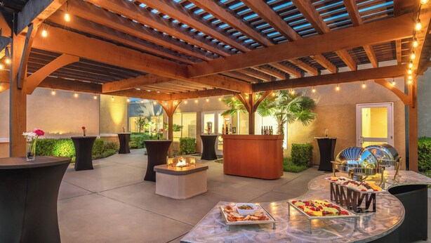 Un patio al aire libre con una pérgola de madera, luces colgantes y una mesa de buffet con diferentes alimentos.