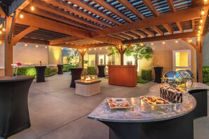 Un patio al aire libre con una pérgola de madera, luces colgantes y una mesa de buffet con diferentes alimentos.
