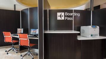 Mostrador de recepción con un letrero que dice 'Boarding Pass', dos sillas de oficina, una computadora e impresora.