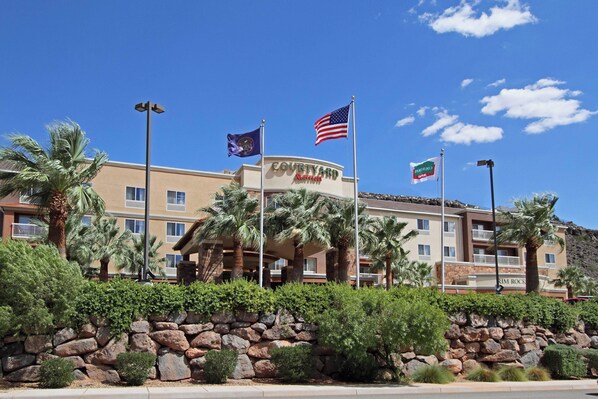 A Courtyard by Marriott hotel with a stone wall, palm trees, and multiple flags. - Courtyard by Marriott St George (St. George)