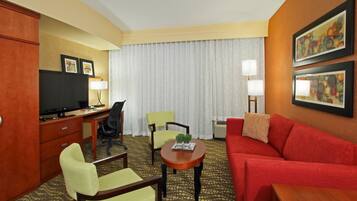 Habitación de hotel con un escritorio, un sofá rojo, dos sillones, un televisor y obras de arte enmarcadas en las paredes.