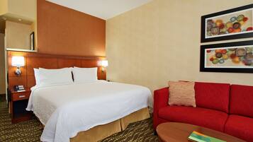 A hotel room with a large bed, a red sofa, a small table, and two framed artworks on the wall.