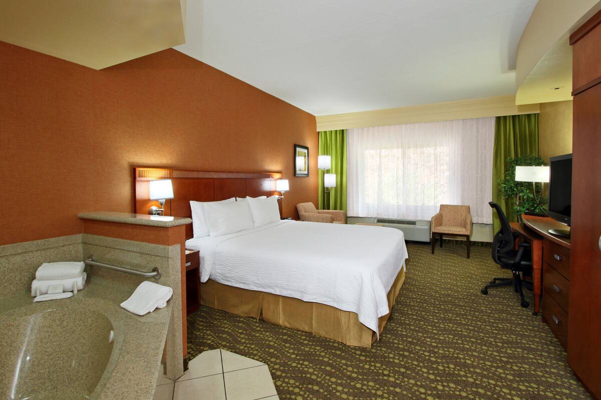 Une chambre d’hôtel comprenant un lit, un bureau, une chaise, une télévision, une lampe, une salle de bain avec une baignoire et une douche.