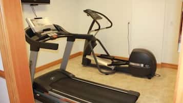 Une salle de sport équipée d’un tapis de course et d’un vélo elliptique, avec un sol recouvert de moquette et un téléviseur fixé au mur.