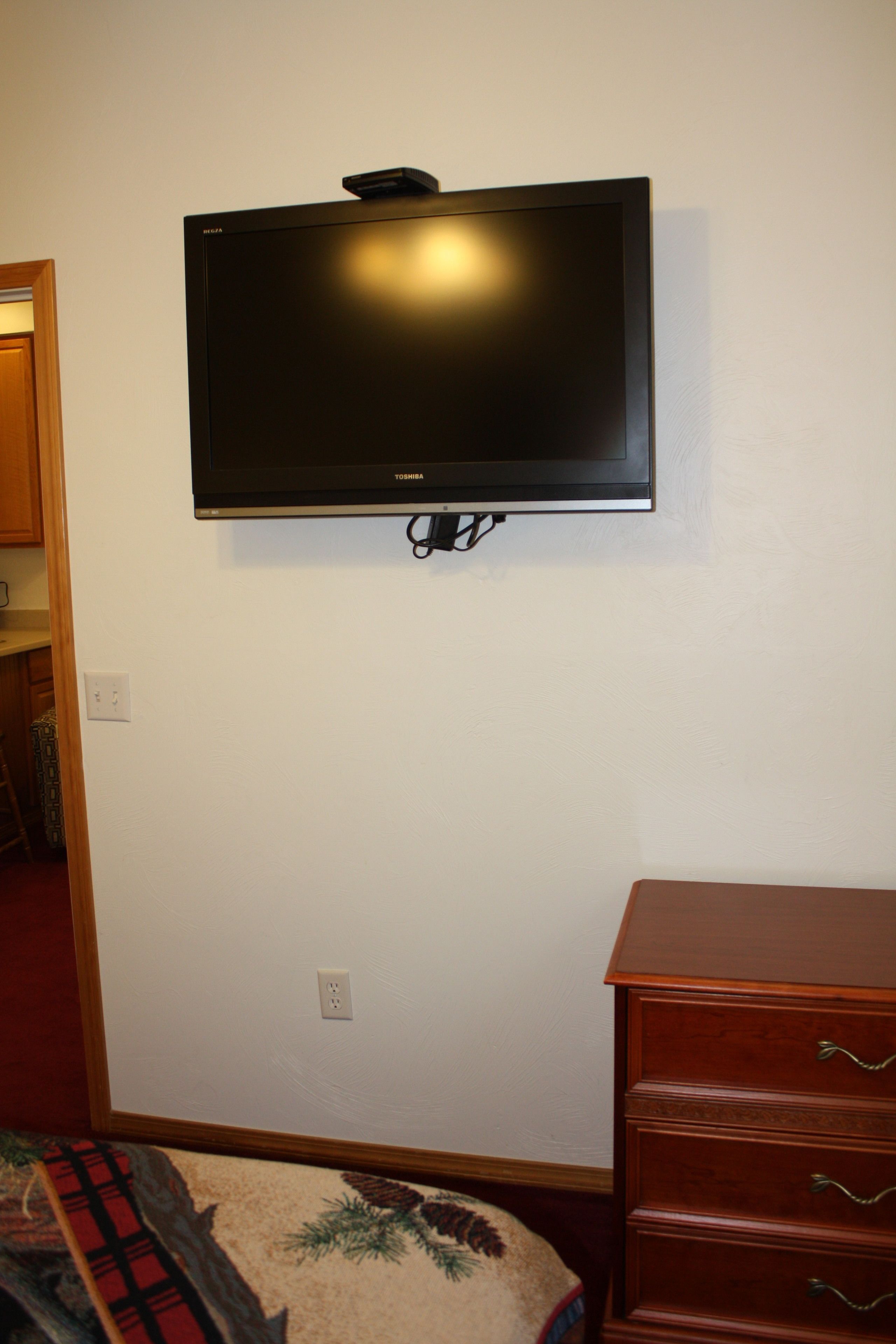 A room with a mounted flat-screen TV on the wall, a wooden dresser, and a carpeted floor.