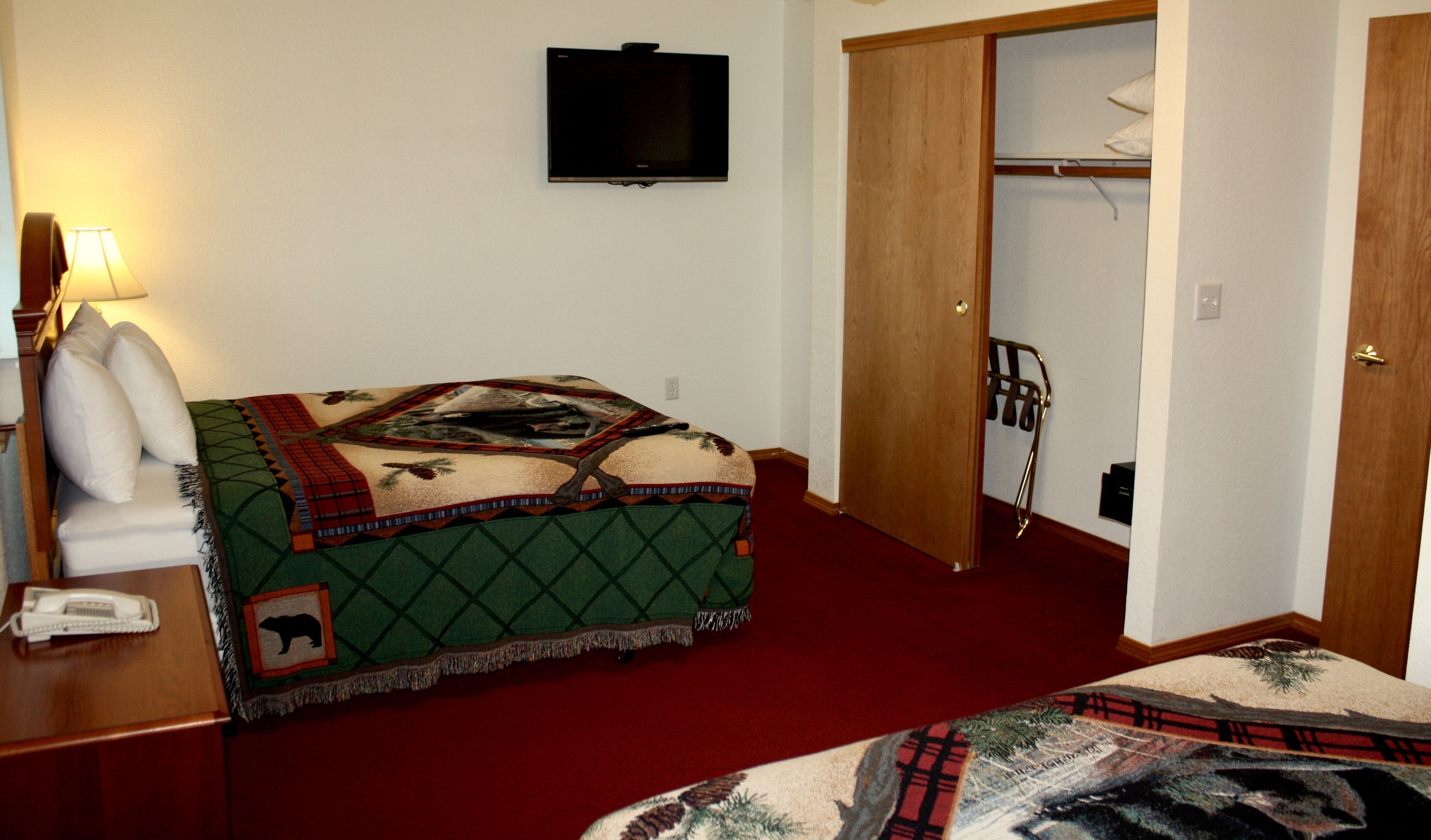 Een hotelkamer met een bed, een aan de muur bevestigde televisie, een nachtkastje met een lamp en een kapstok.
