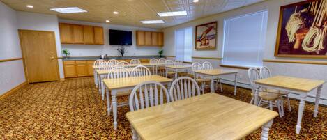 A conference room with multiple tables and chairs, a ceiling with recessed lighting, and a patterned carpet.