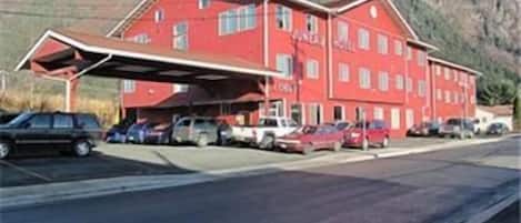 A red building with a covered parking area and a mountainous backdrop.