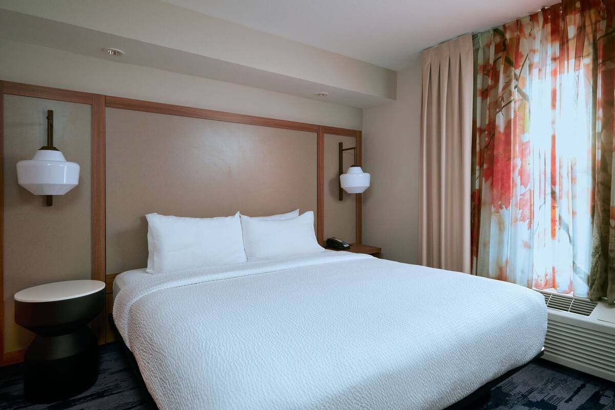 Habitación de hotel con una cama grande, dos mesitas de noche, una lámpara de pared y una ventana con cortinas.