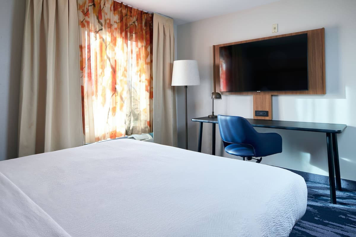 Habitación de hotel con una cama grande, un escritorio con una silla, un televisor de pantalla plana montado en la pared y una lámpara.