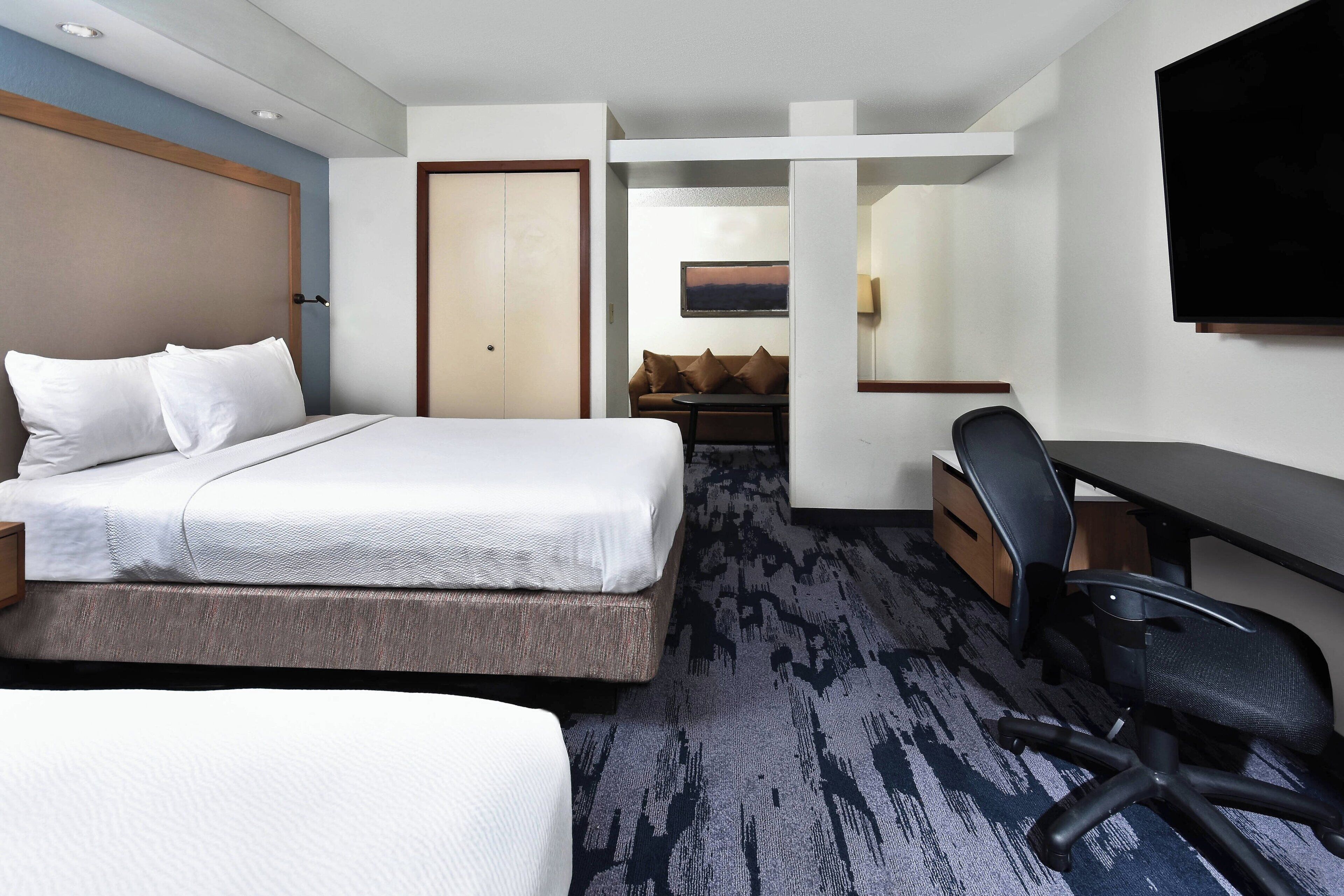 A hotel room with a bed, a desk, a chair, and a television.