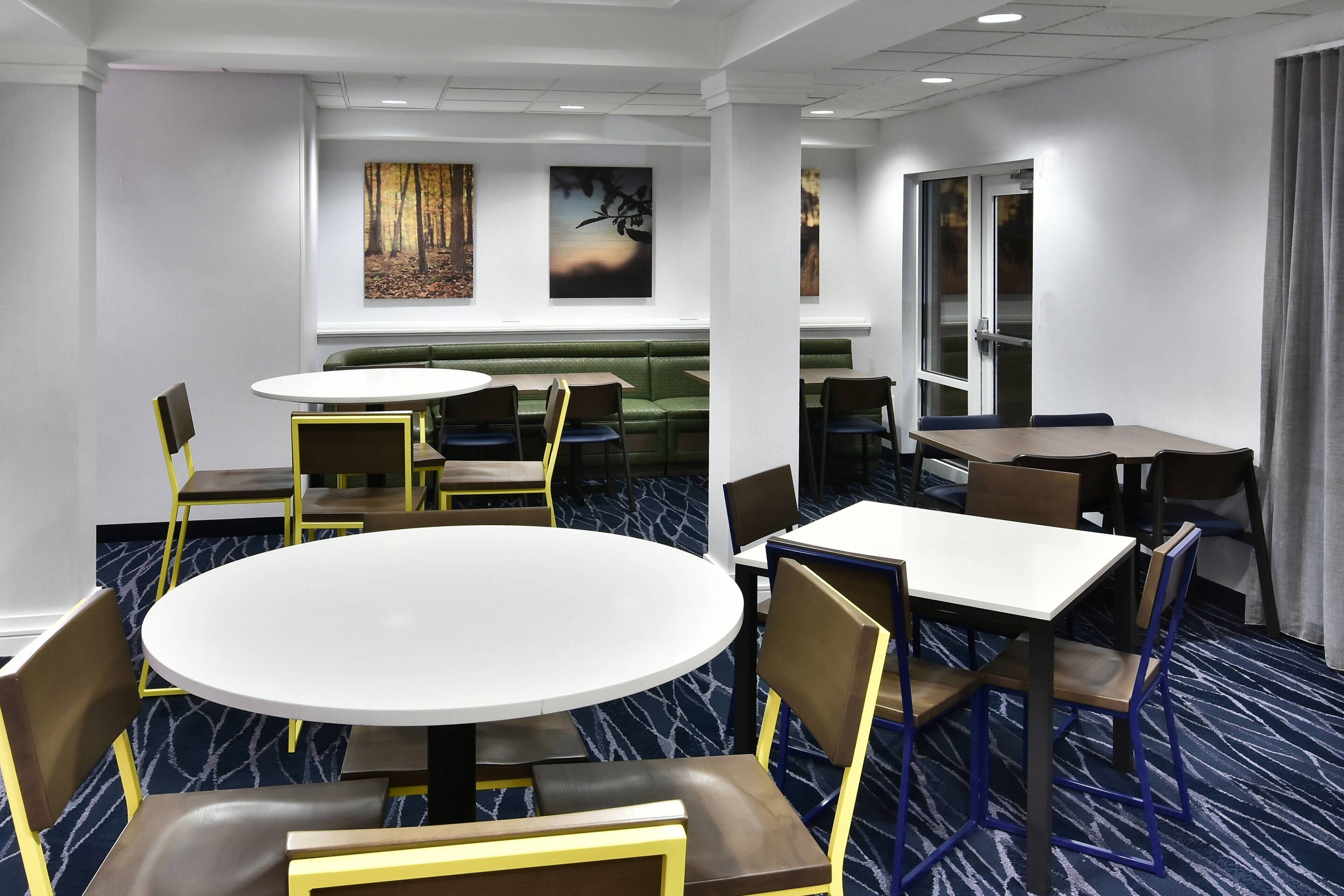 A hotel dining area with round tables, chairs, and a green booth.