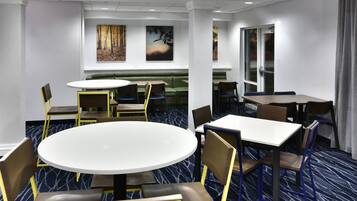 A hotel dining area with round tables, chairs, and a green booth.