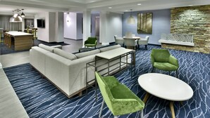 A modern hotel lobby with a sectional sofa, green armchairs, a round table, and a stone accent wall. - Fairfield by Marriott Inn & Suites Richmond Innsbrook (Richmond)