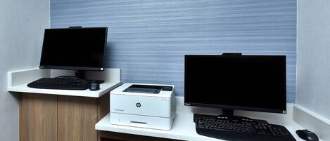 A workspace with two monitors, a printer, and a keyboard on a white desk.