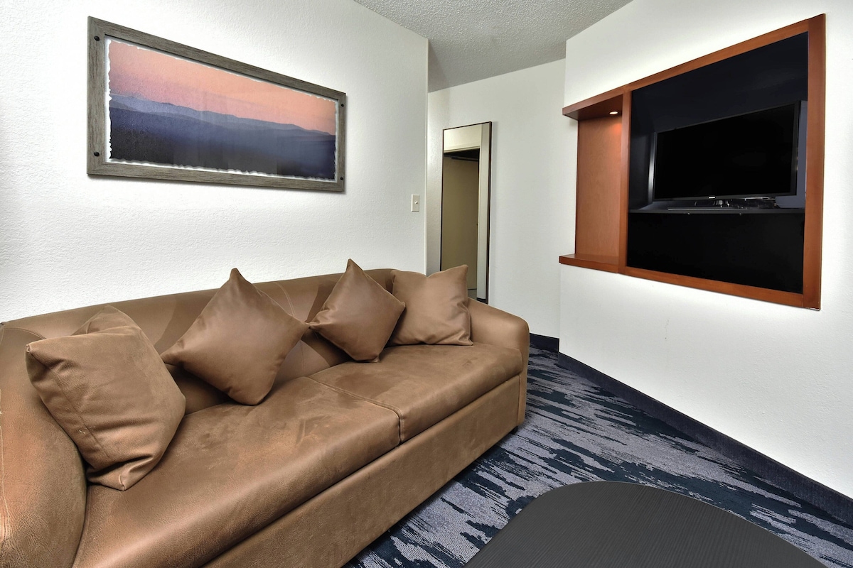 A modern living room with a brown sofa, a mounted TV, and a framed picture on the wall.