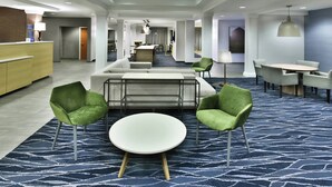 A modern hotel lobby with a reception desk, seating area with sofas and chairs, a central round table, and a dining area with a table and chairs. - Fairfield by Marriott Inn & Suites Richmond Innsbrook (Richmond)