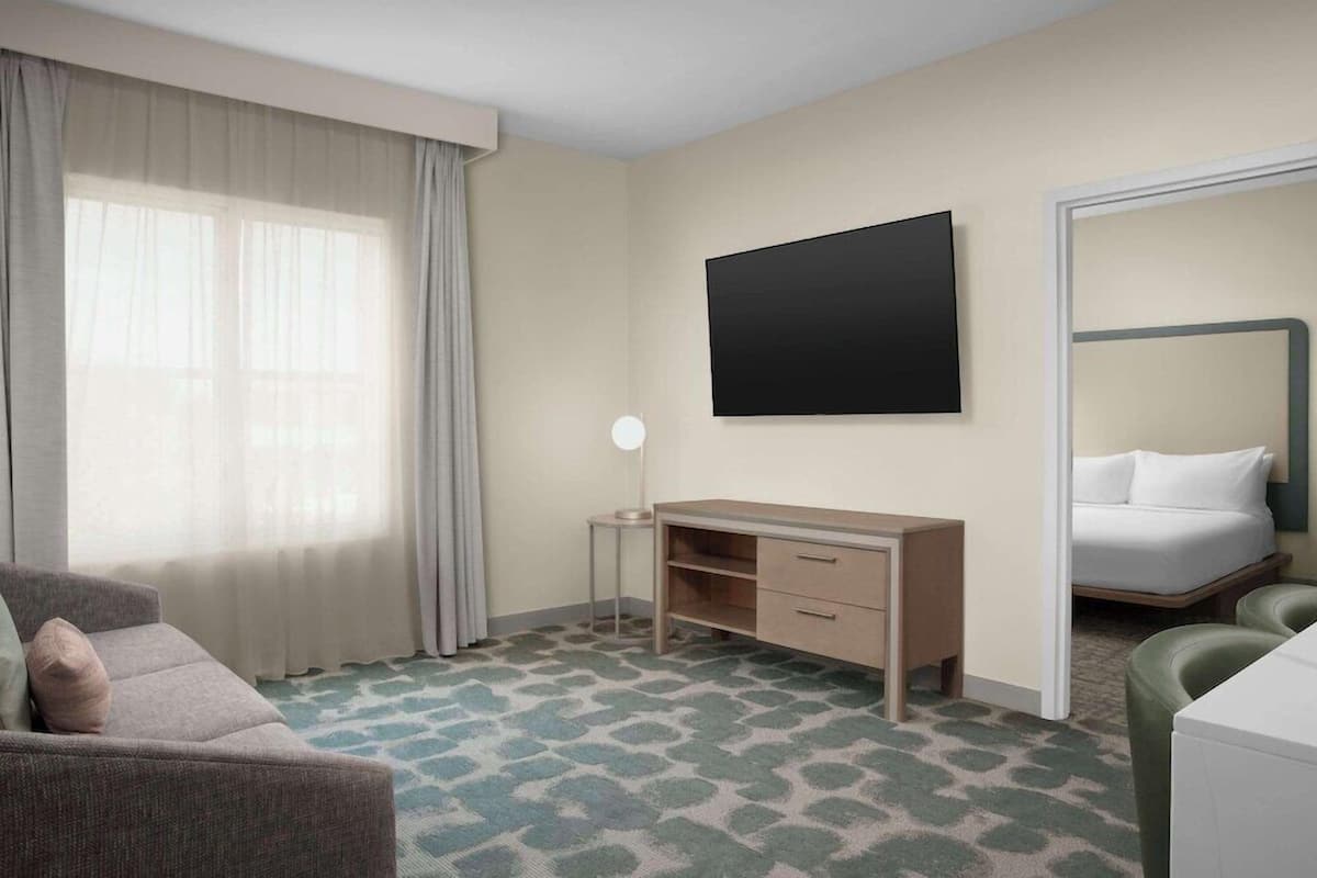 Une chambre d’hôtel avec un lit, un bureau, une chaise, une télévision et une fenêtre avec des rideaux.