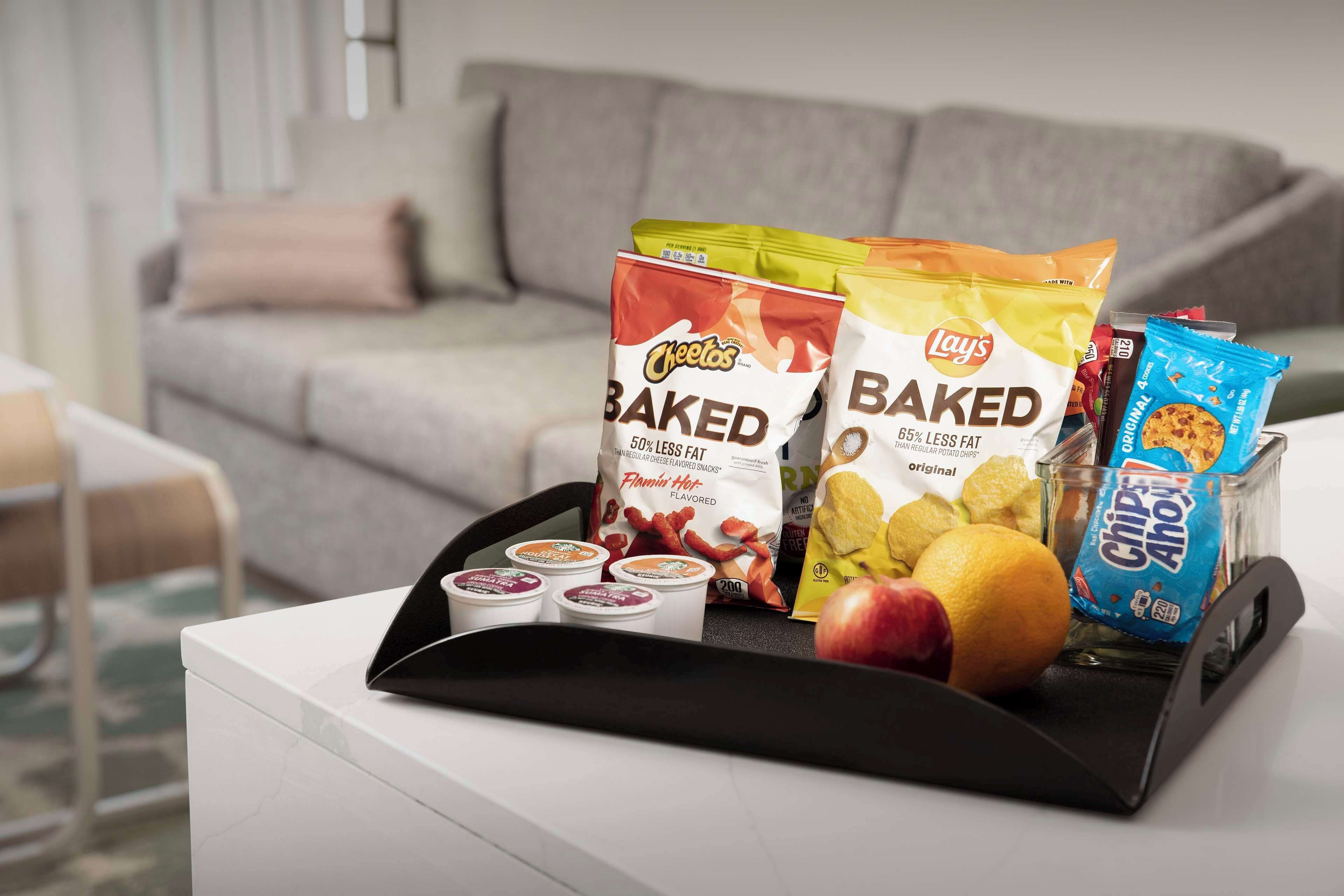 A tray with snacks and a fruit on a white table in a living room with a grey sofa and a beige cushion.
