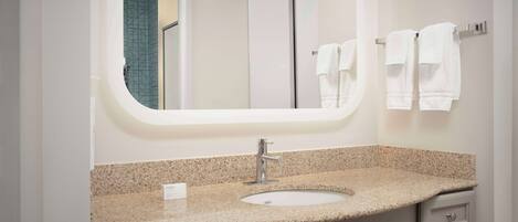 A bathroom with a granite countertop sink, a mirror, and two towels hanging on a towel rack.