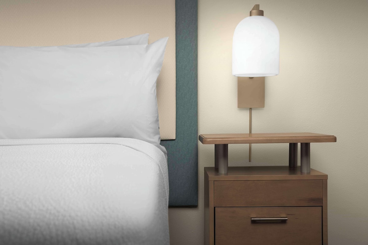 Un lit bien fait avec un oreiller, une table de chevet avec une lampe et une œuvre d’art accrochée au mur.