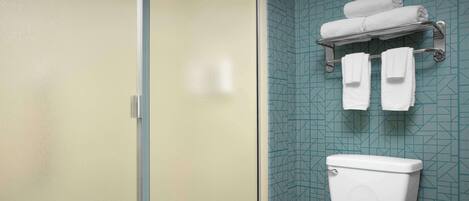 Et badeværelse med toilet, glasvæg til brusebad og et håndklædestativ med håndklæder.