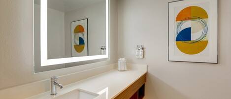 A bathroom with a large mirror, a sink, and a framed abstract painting on the wall.
