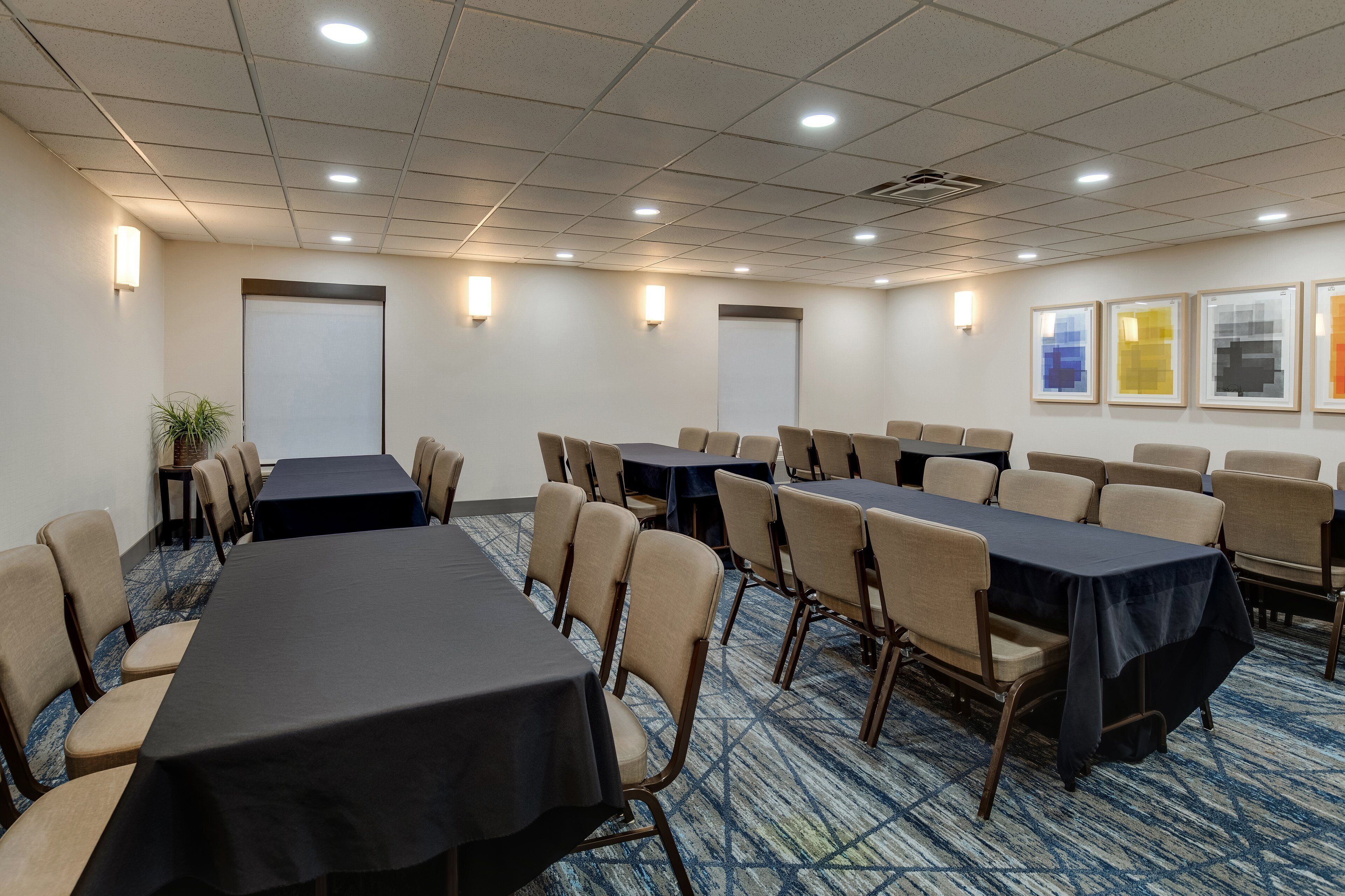 Une salle de conférence dotée de plusieurs tables et chaises, d’un sol recouvert de moquette et de tableaux encadrés accrochés au mur.