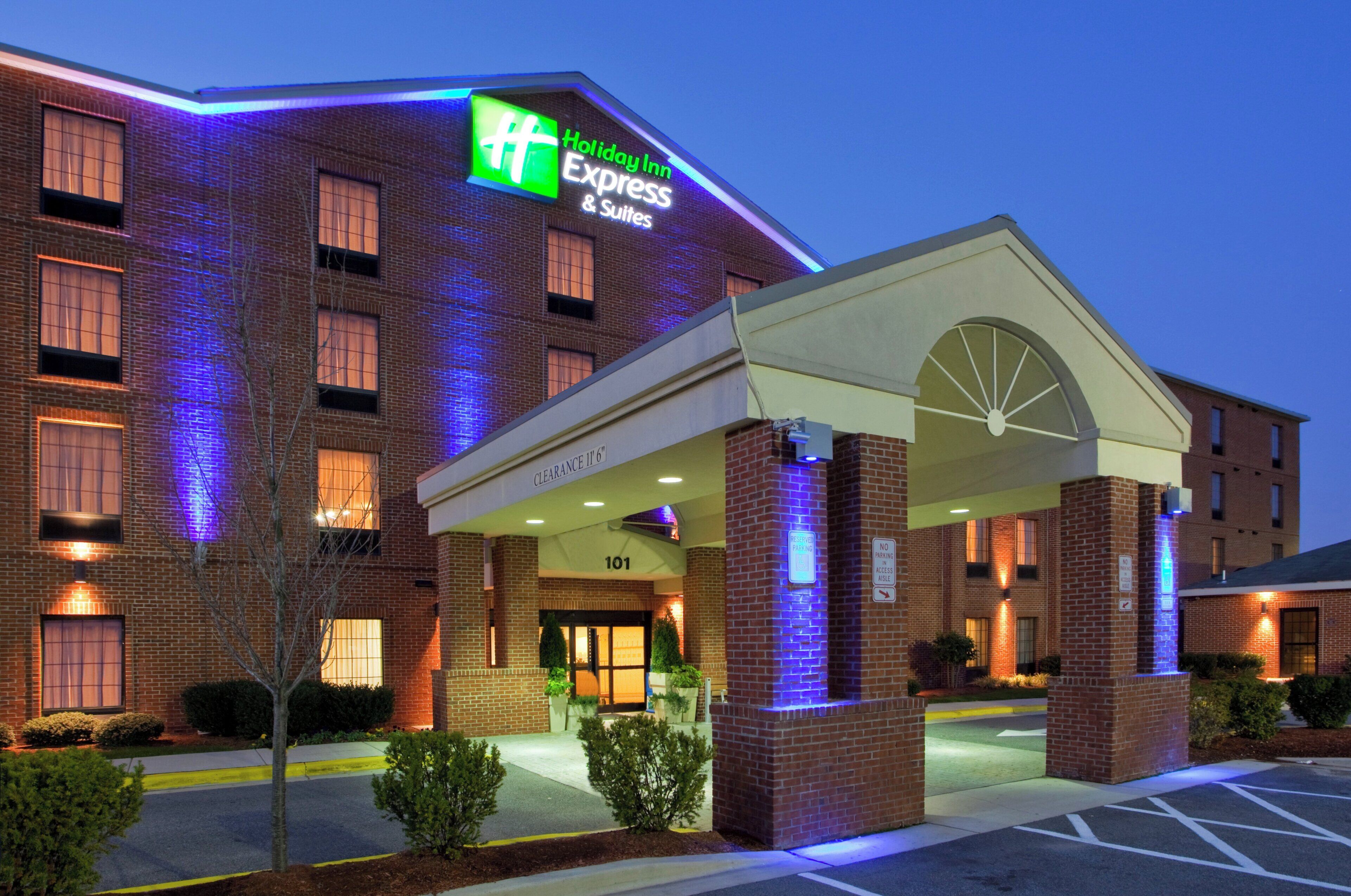 Edificio de Holiday Inn Express & Suites con fachada de ladrillo, entrada iluminada y señalización que indica 'CLEARANCE 11'6' estacionamiento.