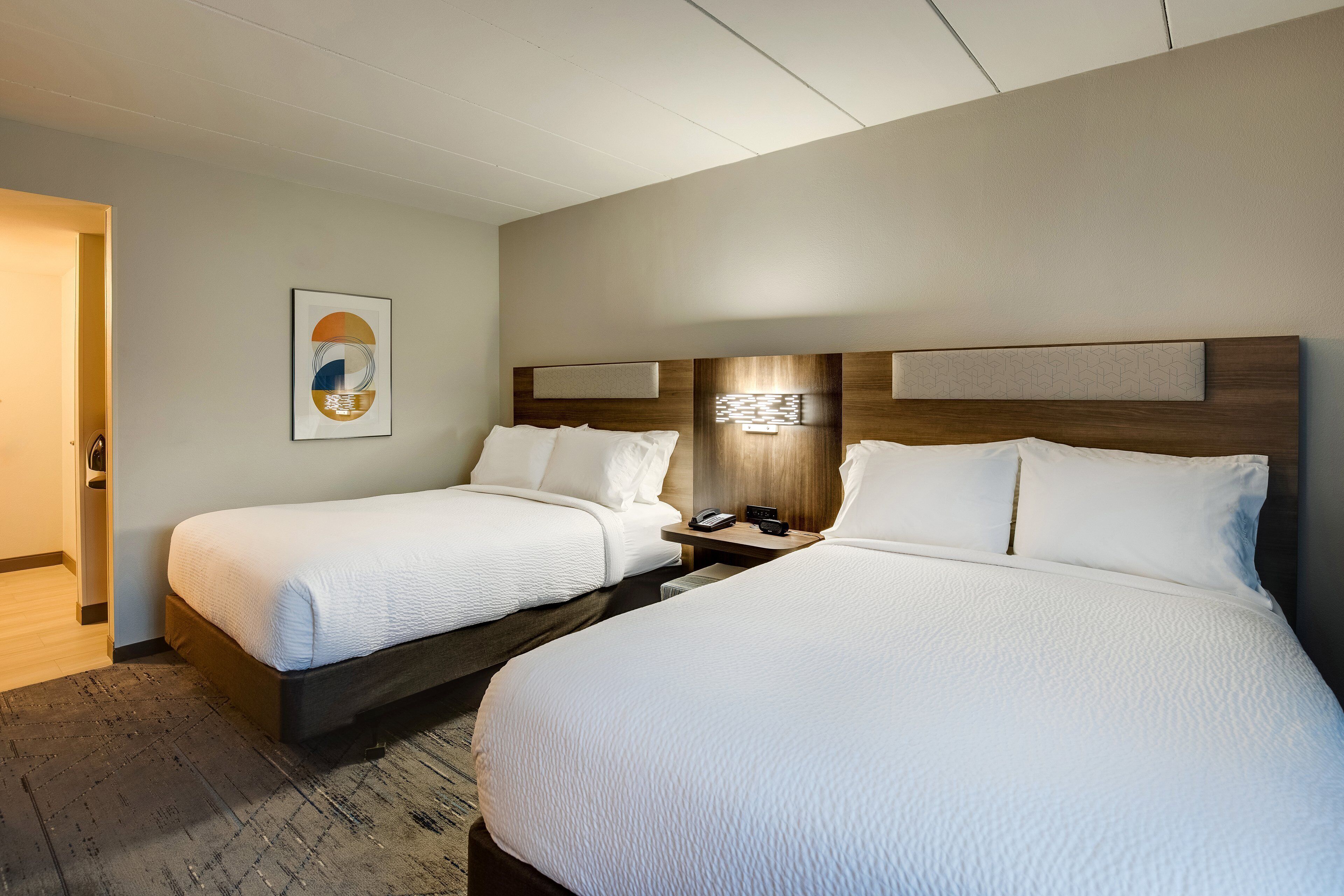 Quarto de hotel com duas camas, uma mesa de cabeceira com luminária e uma obra de arte pendurada na parede.
