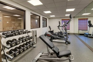 Un gimnasio con racks de pesas, mancuernas y equipo cardiovascular.