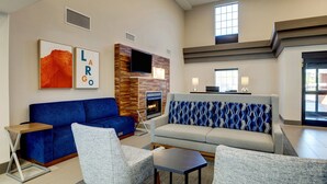 Una sala de estar moderna con un sofá azul, sillones grises y un sofá gris con cojines estampados. Un televisor de pantalla plana está montado en una pared de madera, y debajo hay una chimenea.