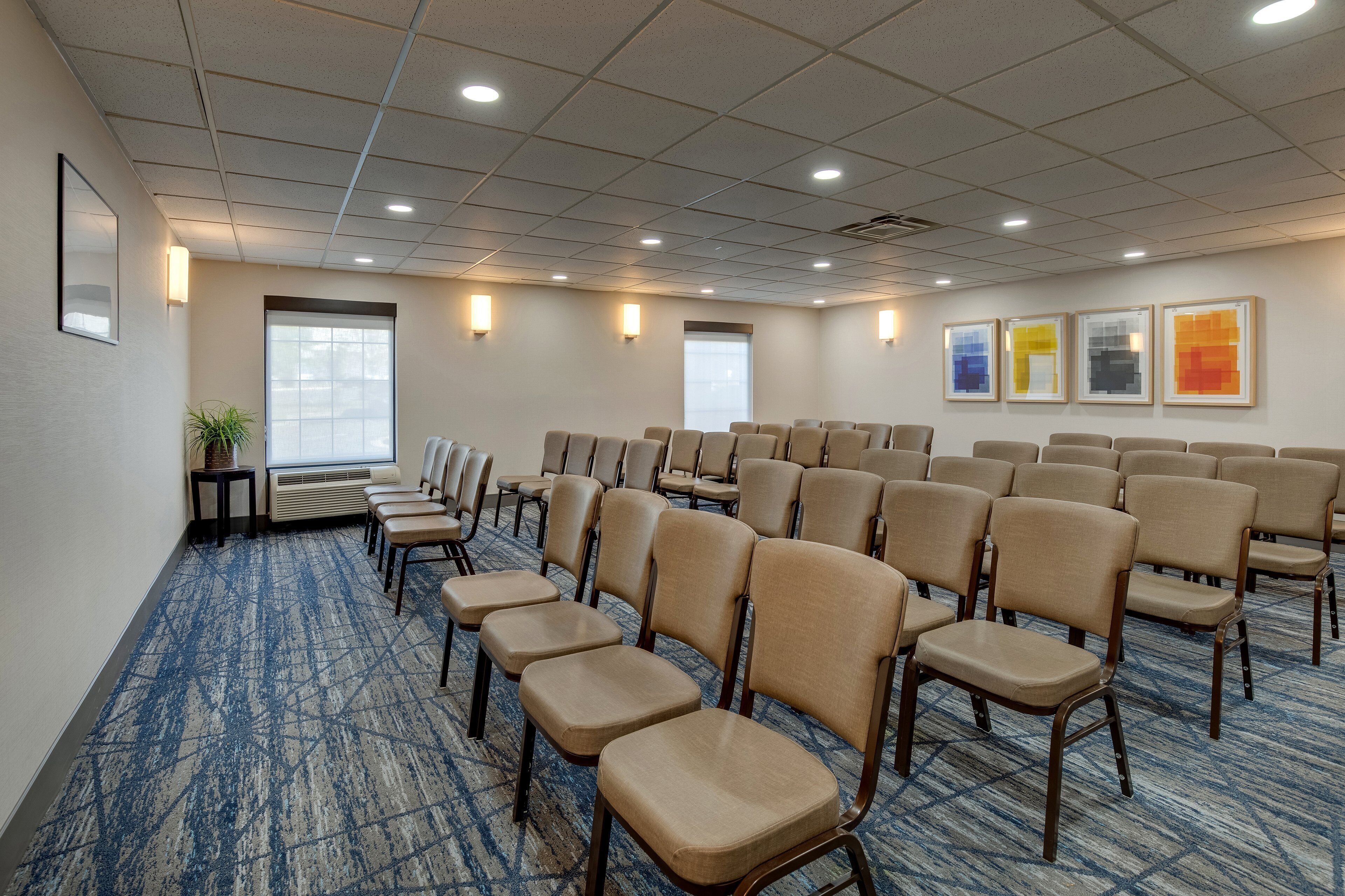 Un salón de conferencias con filas de sillas color beige, piso alfombrado y cuadros en las paredes.