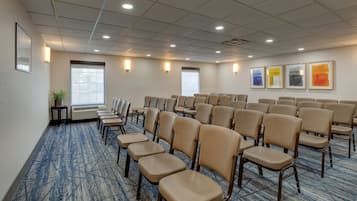 Un salón de conferencias con filas de sillas color beige, piso alfombrado y cuadros en las paredes.