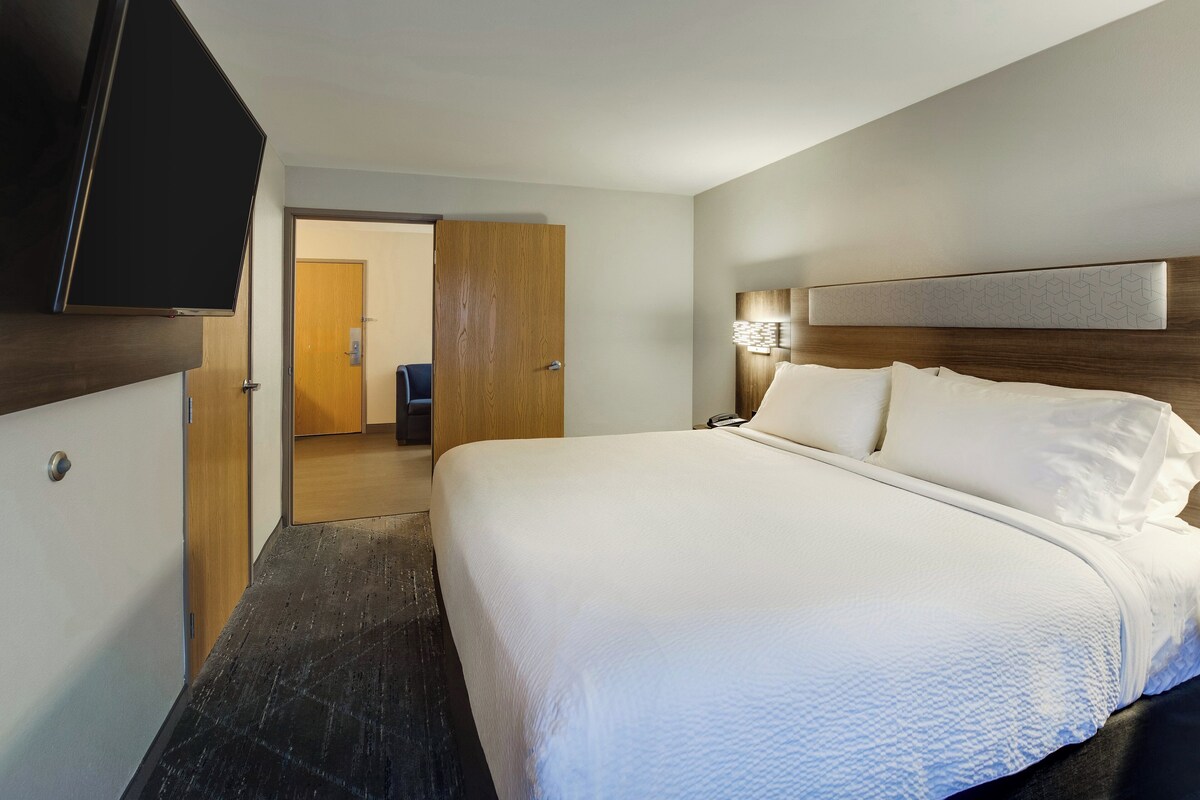 A hotel room with a large bed, a television mounted on the wall, and a wooden door leading to another room.