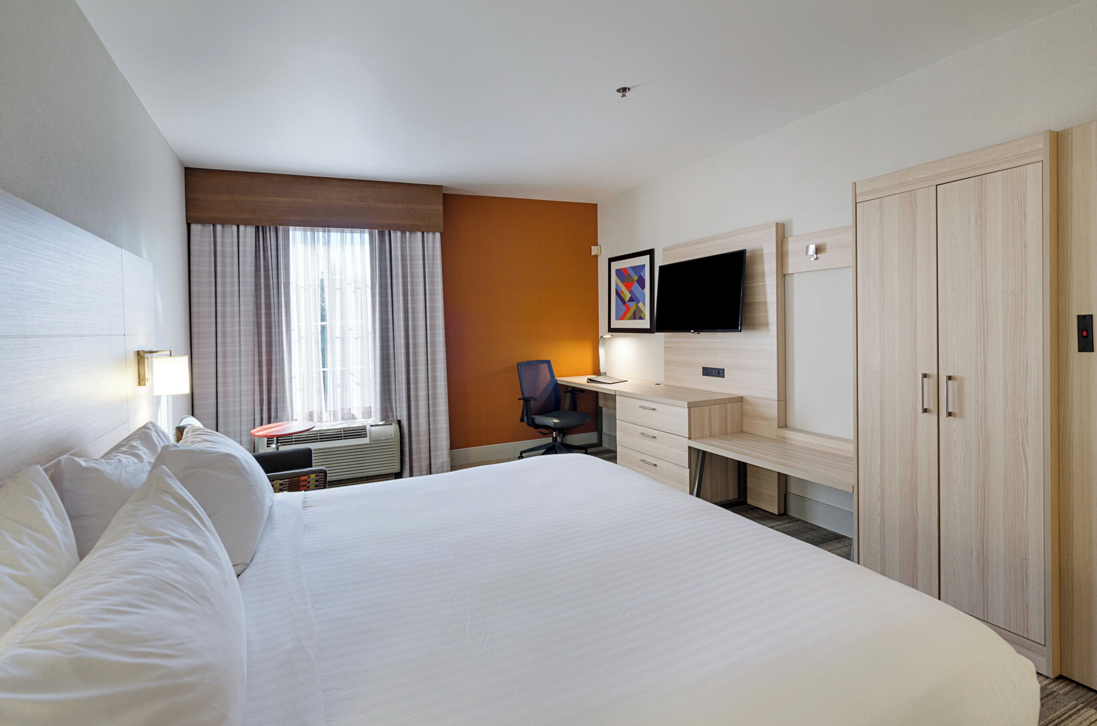 A hotel room with a large bed, a desk with a chair, a television, and a wardrobe.