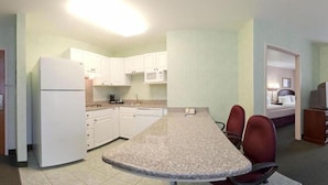 A compact kitchen with white cabinets, a microwave, and a refrigerator. There is a granite countertop with two chairs.